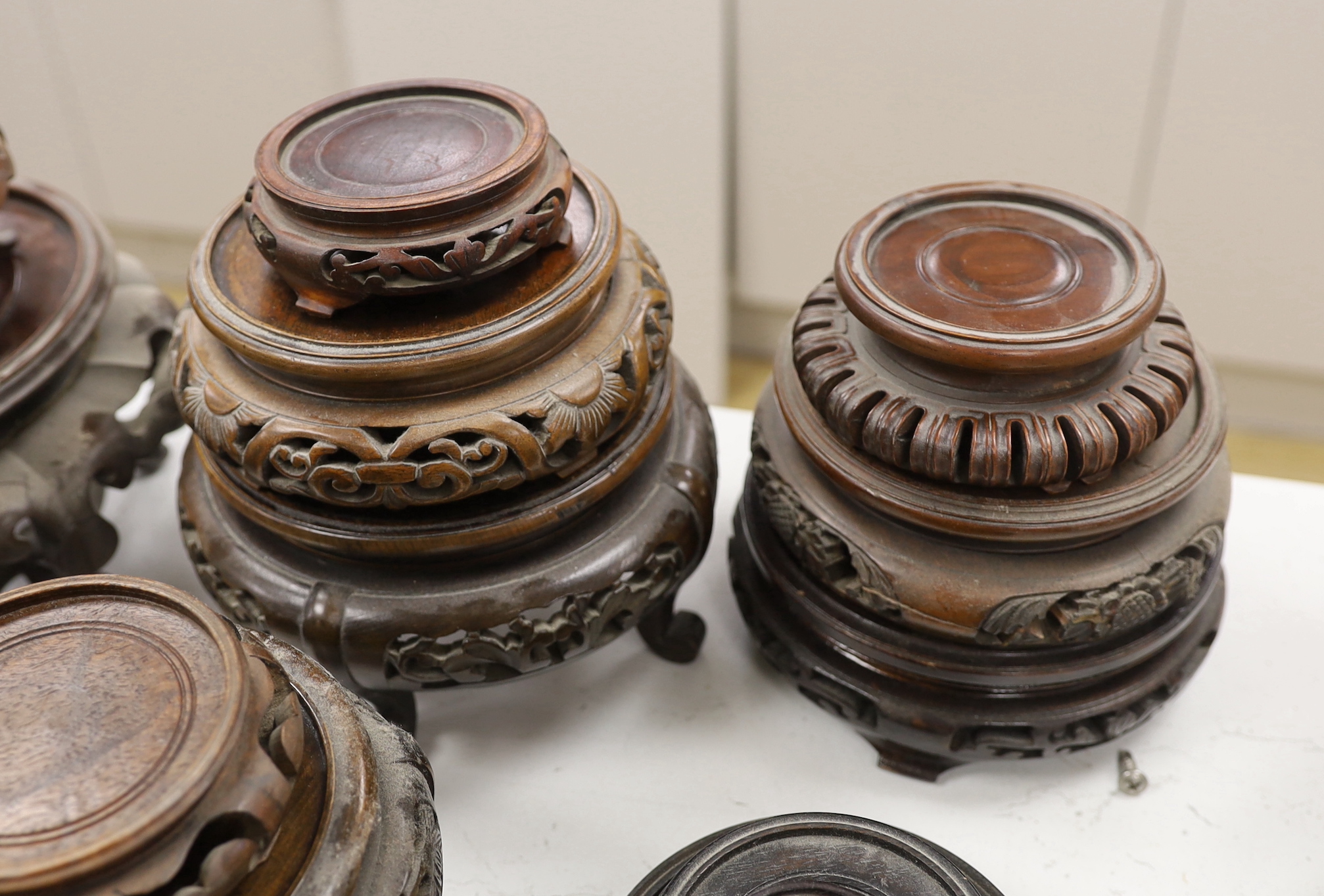 Twenty five assorted Chinese hardwood vase stands and two carved wooden vase covers, largest stand 22cm diameter